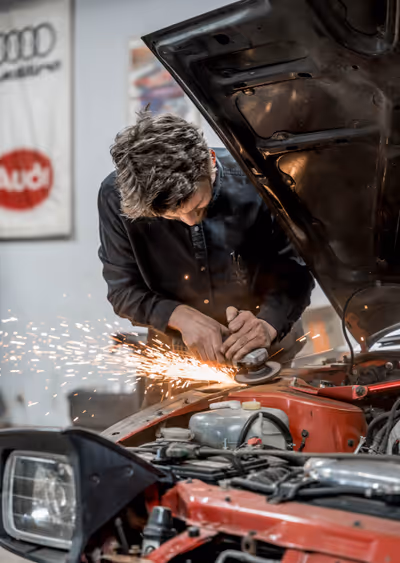 Dan grinding in a red car engine bay