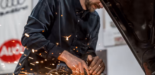 Technician grinding and shaping metal panel during custom fabrication